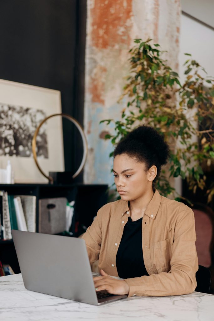 Young woman with curly hair working on a laptop in a cozy home office environment.